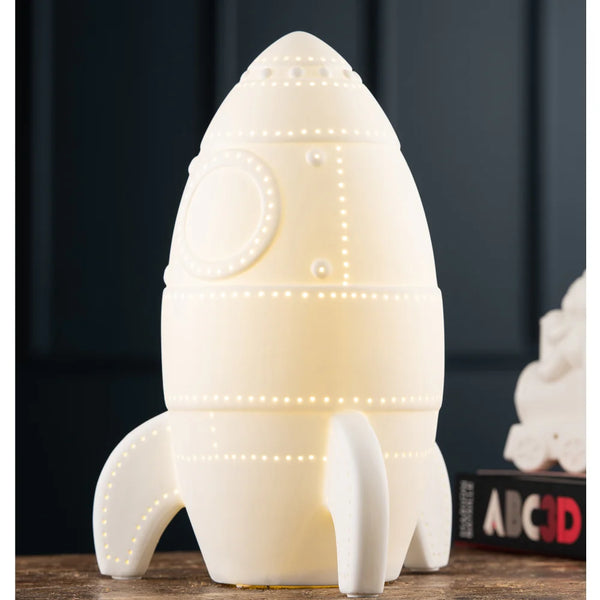 Rocket-shaped white ceramic LED lighthouse with small perforated light details on a wooden surface.