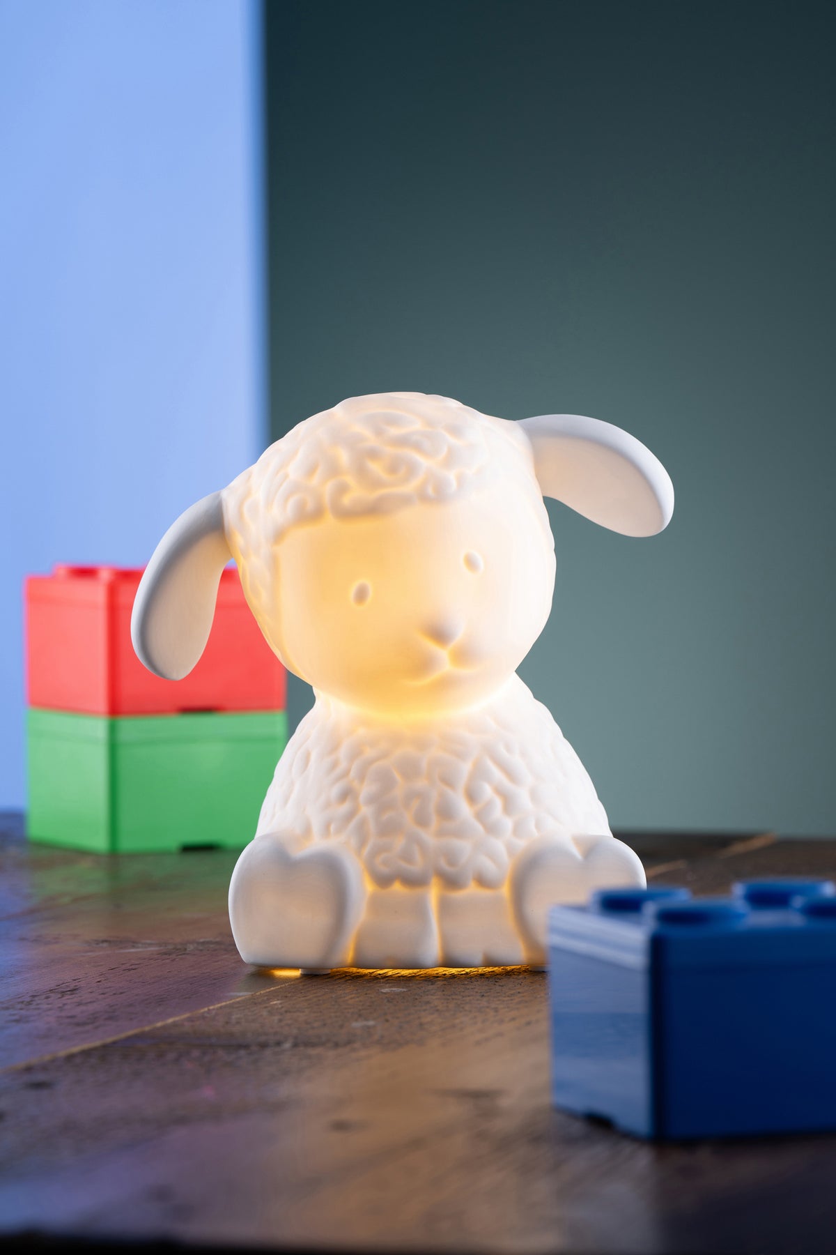 Glowing white ceramic Christmas Lamb Luminaire on wooden surface with colorful blocks in background