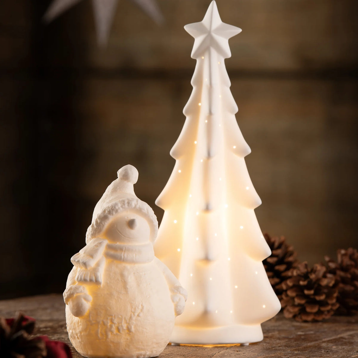 White ceramic Belleek Snowman LED with scarf and hat beside a lit ceramic Christmas tree with star topper.