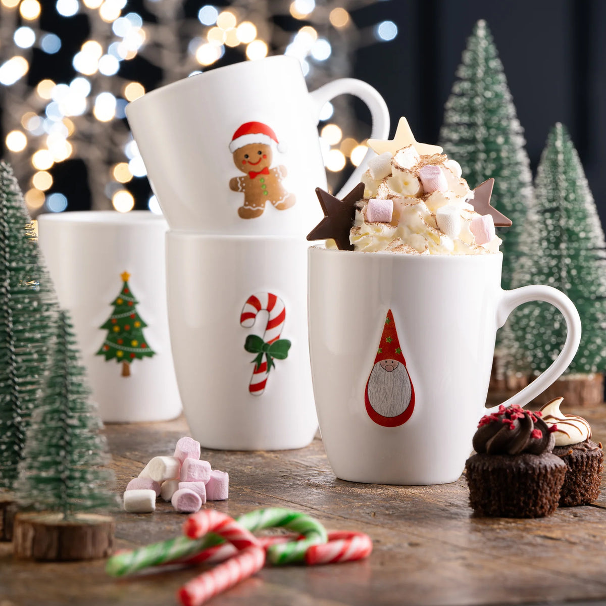 Set of four white Christmas mugs with embossed gingerbread, Santa, candy cane, and tree motifs on wooden table with treats.