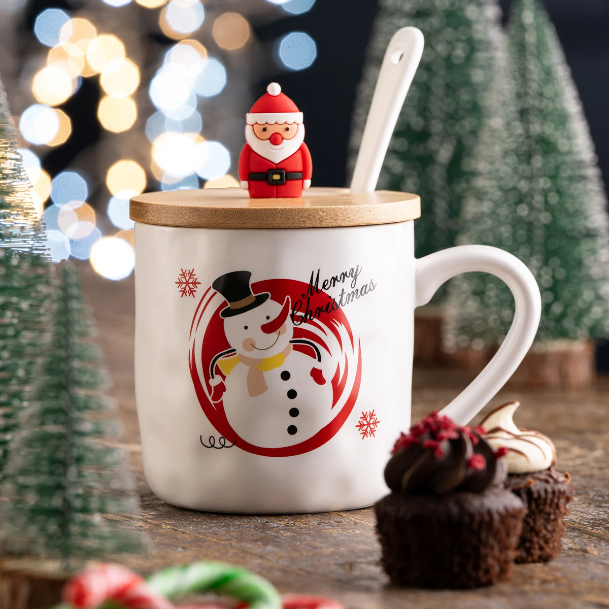 White mug with snowman and "Merry Christmas" text, bamboo lid topped with Santa figure, and white spoon inside.