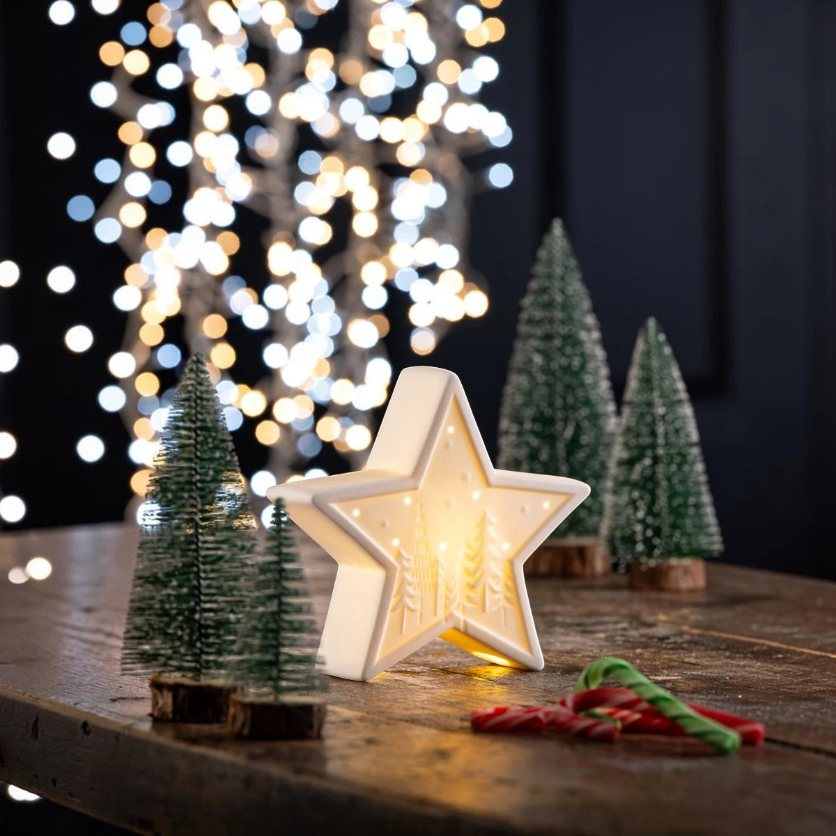 Belleek Star LED light with tree and star cutouts, glowing warmly on a wooden table with mini trees and candy canes.