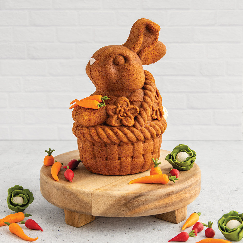 Toffee bunny-shaped cake in a basket design on a wooden stand with decorative carrots and cabbages.