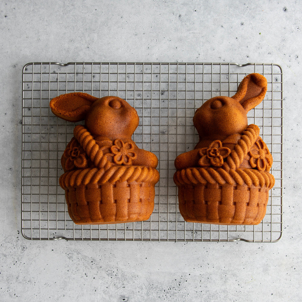 Two toffee-colored bunny cakes in basket shapes cooling on a wire rack against a gray surface.