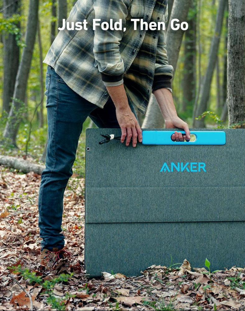 Person holding folded Anker 531 Solar Panel (400W) by its blue handle in a forest setting.