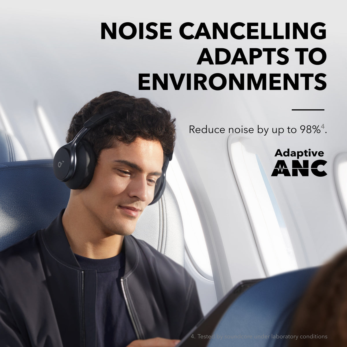 Young man wearing black Soundcore Space One headphones on an airplane seat, using a tablet.