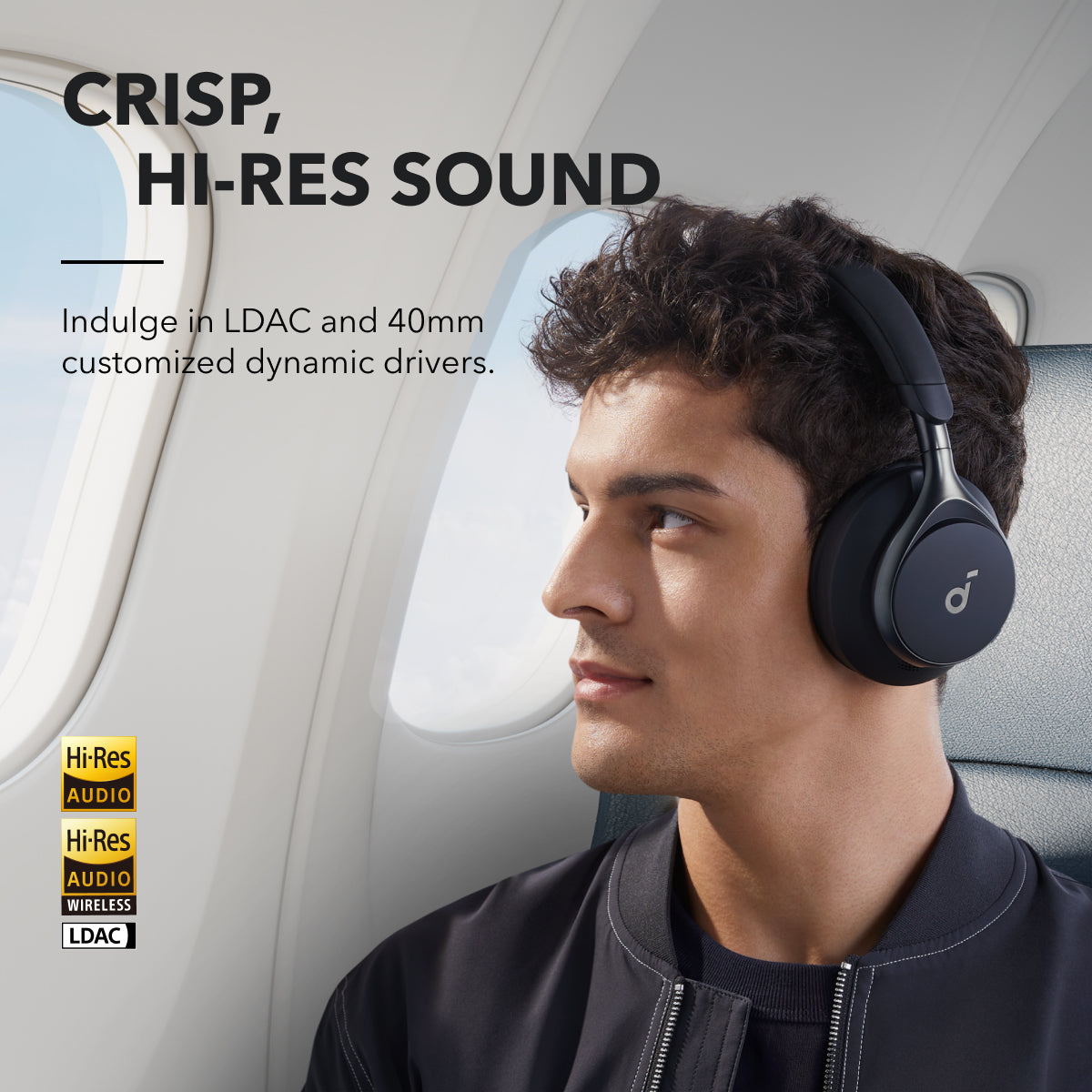 Man wearing black Soundcore Space One headphones sitting by an airplane window looking right.