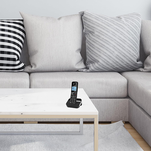 Alcatel F860 cordless phone on a white coffee table in front of a gray sectional sofa with patterned cushions