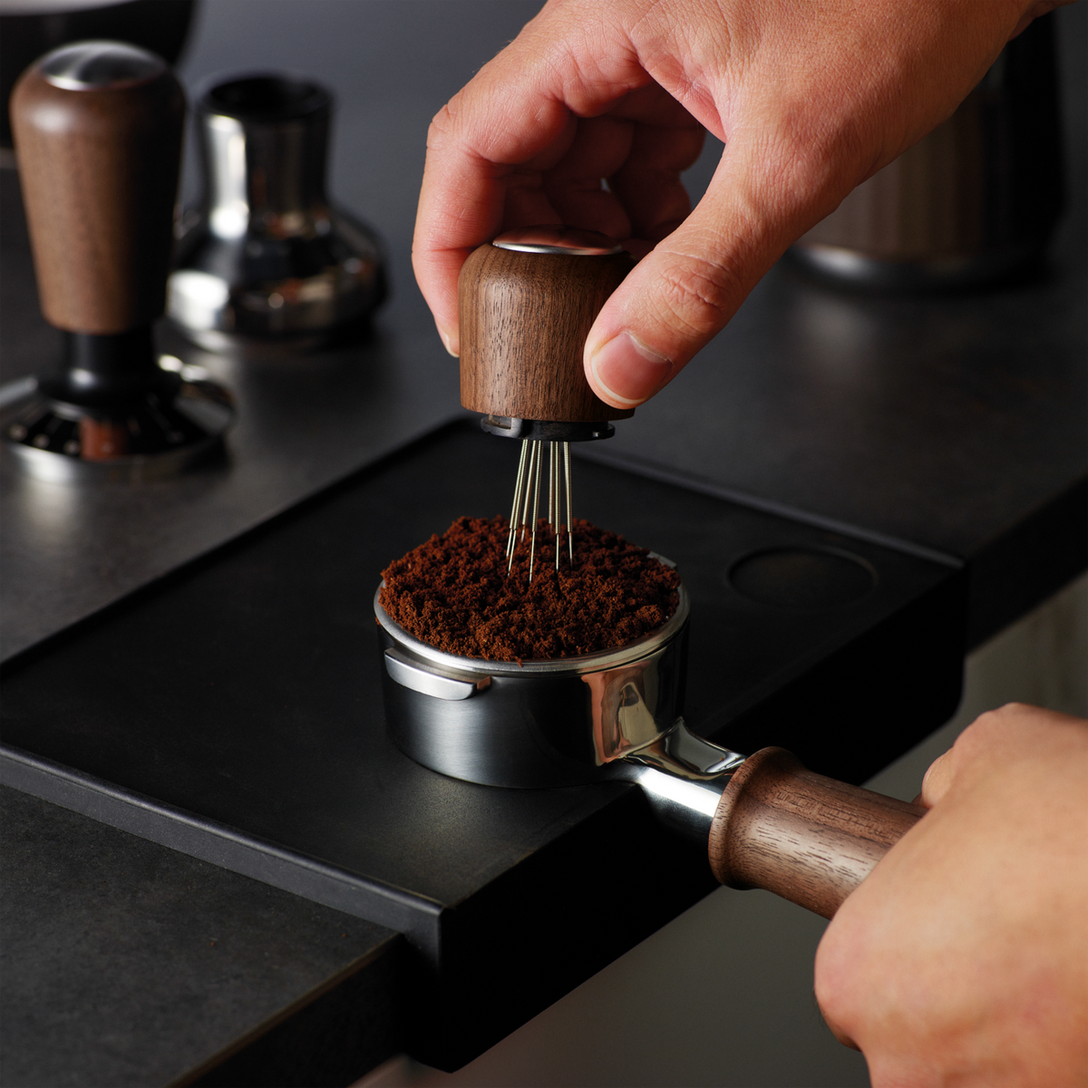 Hand using Sage the Distribution Duo 58mm to evenly distribute coffee grounds in a portafilter.