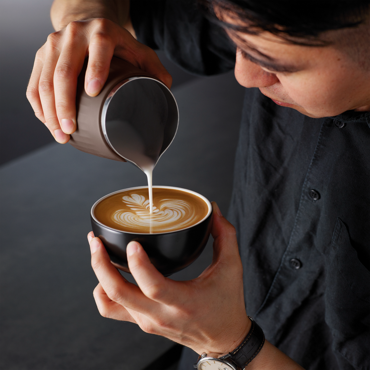 Person pouring milk from the brown Sage the Pro Control Jug into a cup of latte with latte art.