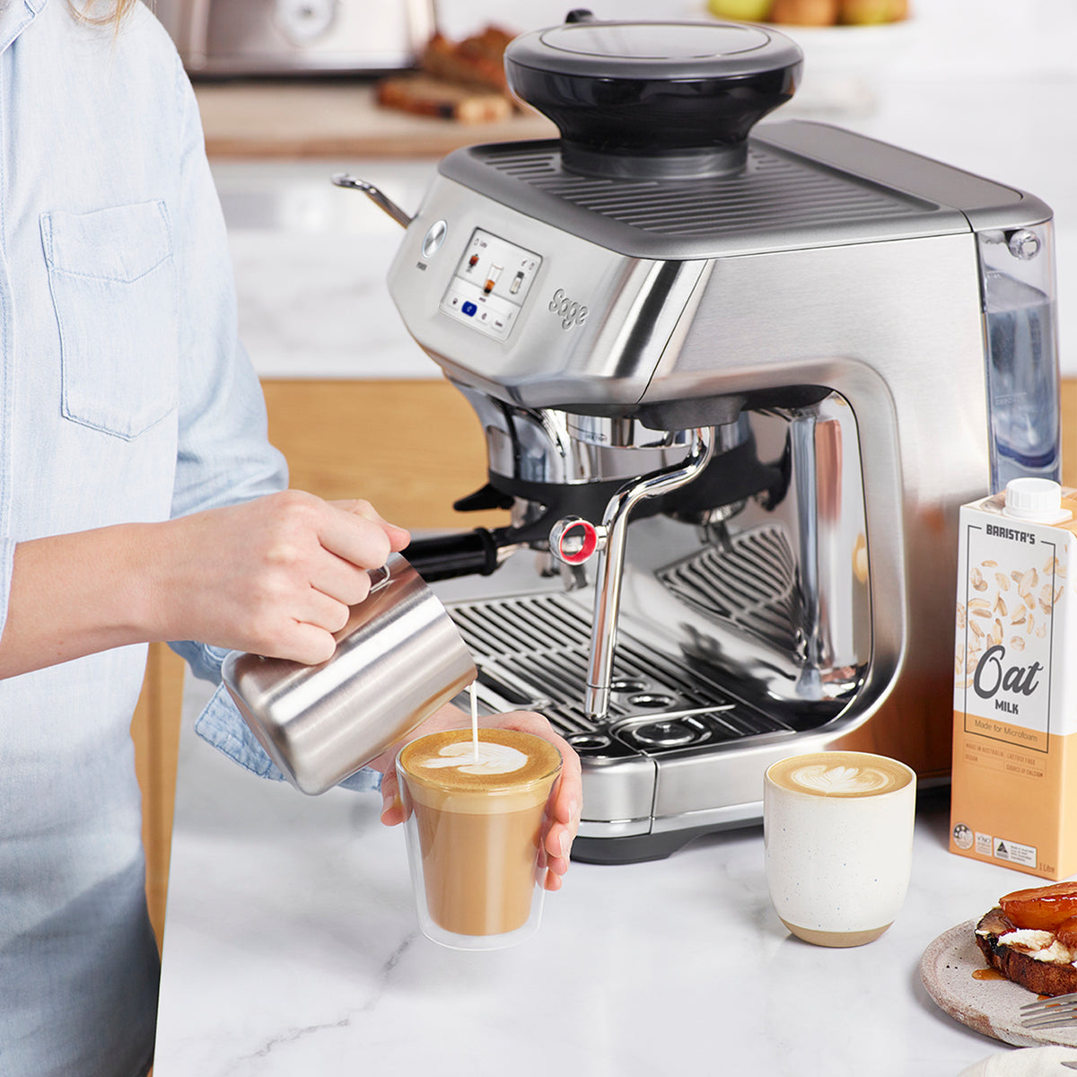 Sage Barista Touch Impress stainless steel espresso machine with person pouring milk into coffee cup