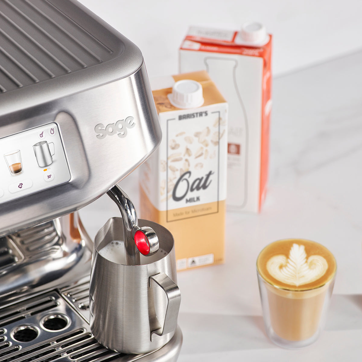 Close-up of Sage Barista Touch Impress stainless steel steaming milk with latte art and oat milk cartons nearby