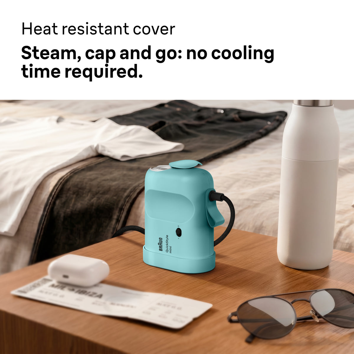Braun Carestyle Mini Travel Garment Steamer in green on a wooden table with sunglasses and a water bottle nearby