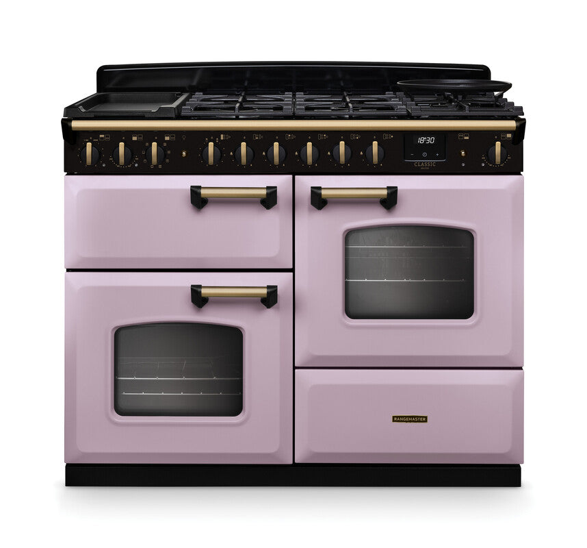 Rangemaster Classic Deluxe 110 dual fuel cooker in pastel pink with antique brass handles and black control panel