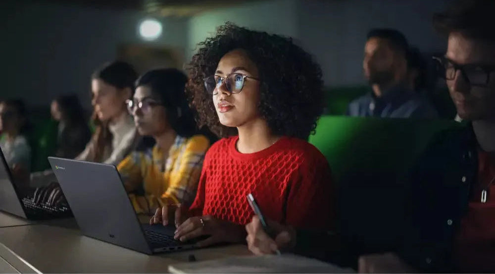 Asus 14" HD Chromebook in grey open on a desk with a woman in a red sweater using it in a classroom setting