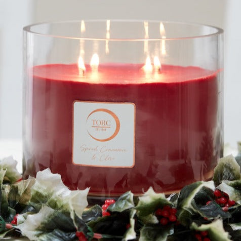 Large Torc Candles Cinnamon Spice 4-wick candle burning in clear glass jar surrounded by holly leaves and berries
