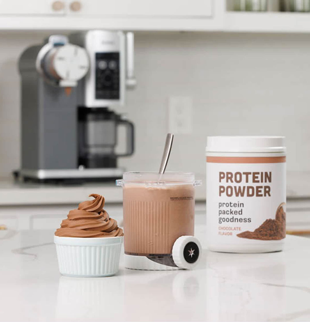 Ninja Swirl soft serve machine container with chocolate soft serve, mixing cup, and protein powder tub on kitchen counter