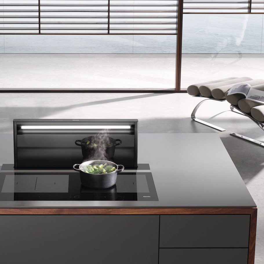 Miele DAD 4841 downdraft extractor raised behind a black induction cooktop with a steaming pot of broccoli.