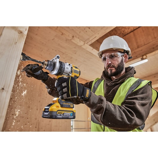 Man wearing safety gear using DeWalt 18V XR Brushless Premium Hammer Drill Driver on wood panel
