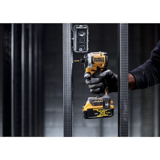 DeWalt 18v compact 1/4 inch impact driver held by a gloved hand between metal studs in a construction setting