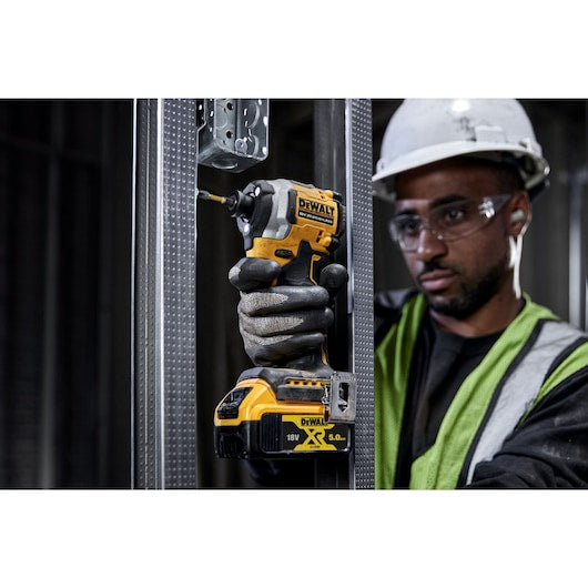 DeWalt 18V Compact 1/4 Inch Impact Driver in use, held by a worker wearing safety gear.