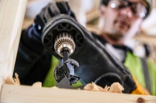Close-up of a DeWalt 35mm self-feed drill bit attached to a drill, cutting into wood.