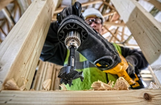 Close-up of a DeWalt 35mm self-feed drill bit attached to a drill, cutting into wood framing.