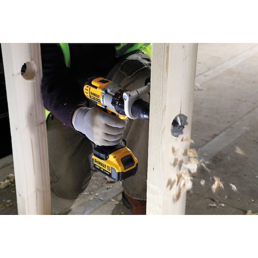 DeWalt drill with 41mm self-feed drill bit boring a hole through wooden beam, wood chips flying.