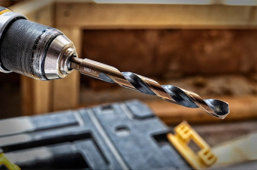 Close-up of a DeWalt black and gold metal drill bit attached to a drill in a workshop setting.