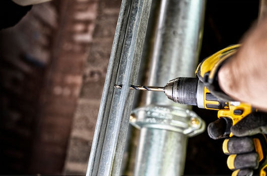 Person using a yellow and black drill with a metal drill bit on a metal pipe or beam.