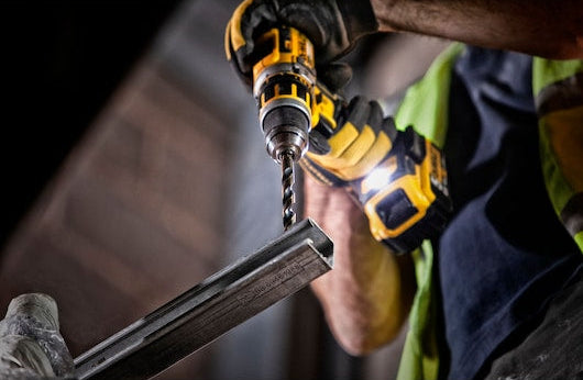 Person using a DeWalt drill with a black and gold metal drill bit on a metal beam.