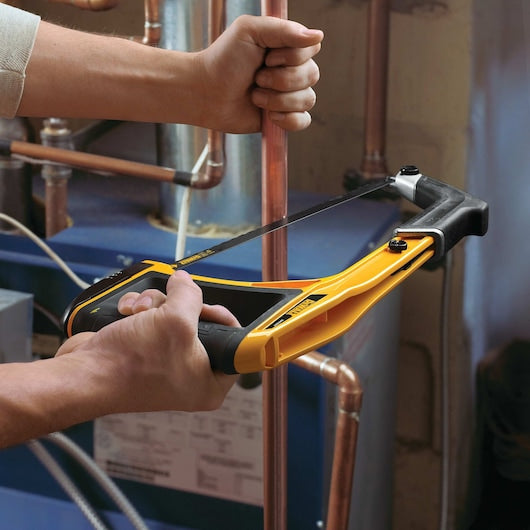 Hands using a DeWalt 5-In-1 Hacksaw with a 300mm blade to cut a copper pipe in a plumbing setting.
