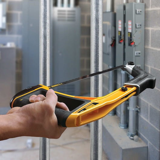 Hand holding a DeWalt 5-In-1 Hacksaw with 300mm blade cutting metal pipes in an industrial setting.