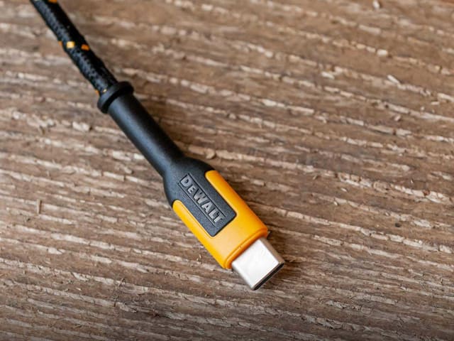Close-up of DEWALT USB C connector with black and yellow reinforced cable on wooden surface.