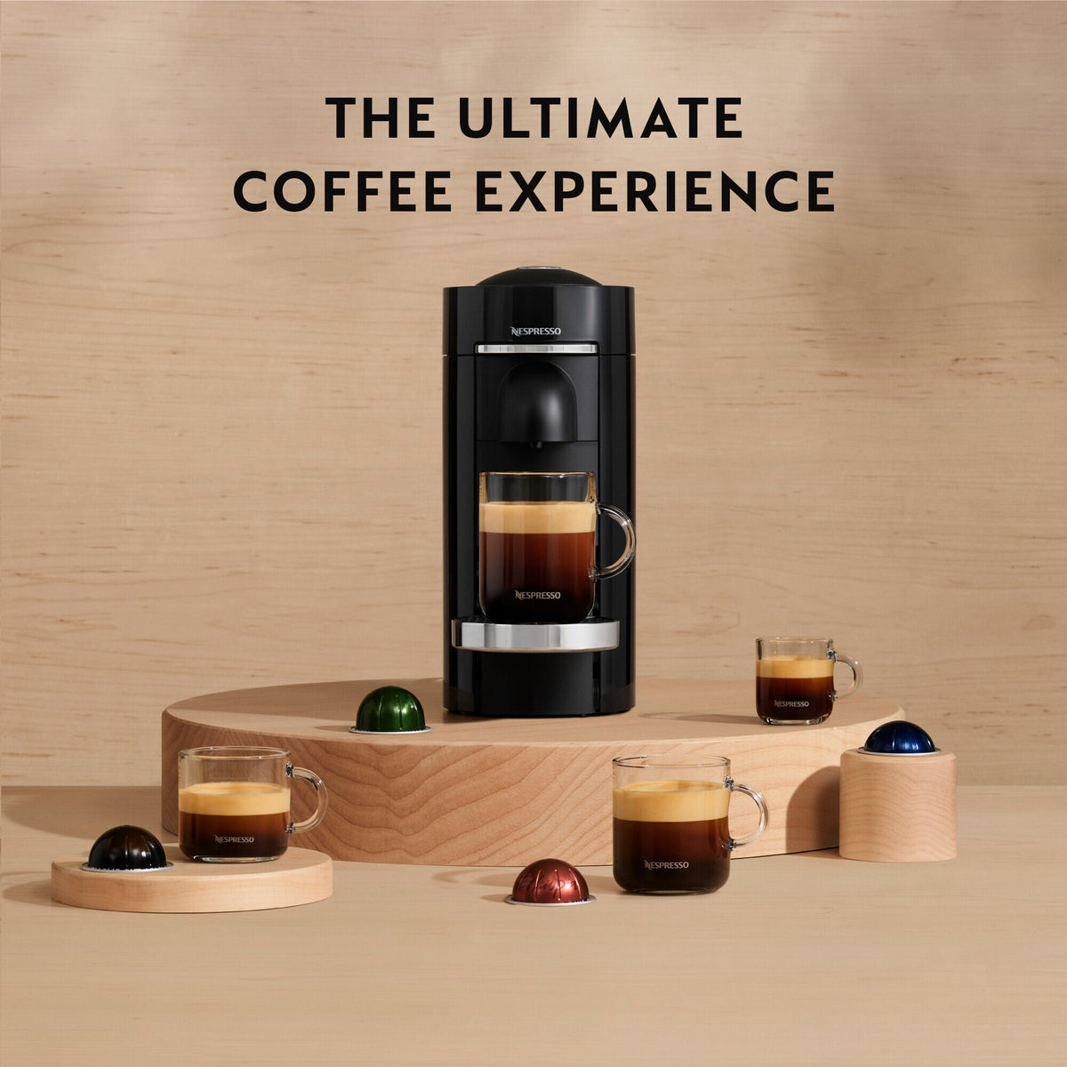 Delonghi Nespresso Vertuo Plus black coffee machine with four glass cups and colorful coffee capsules on wooden stands.
