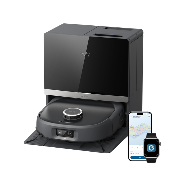 A dark gray robotic vacuum cleaner docked in its charging station, shown on a clean white background with a smartphone and smartwatch displaying companion app interfaces.