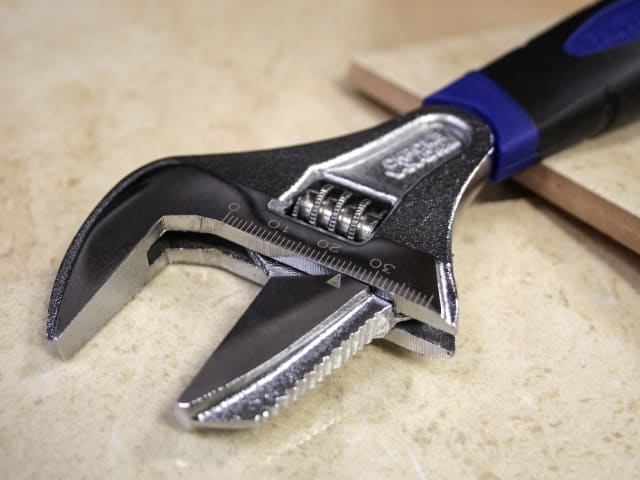 Close-up of adjustable spanner with wide mouth and blue-black handle on a beige surface.