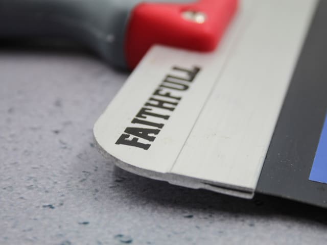 Close-up of Faithfull drywall taping knife blade with logo and part of red and black handle visible.