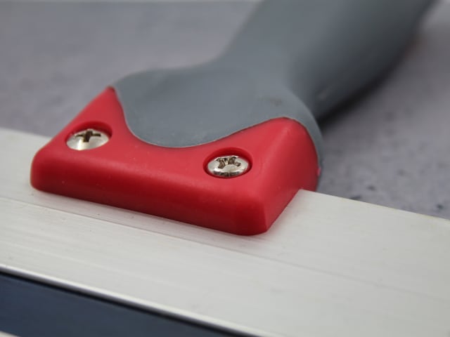 Close-up of the red and grey handle attached with screws to the blue steel blade of the drywall taping knife.