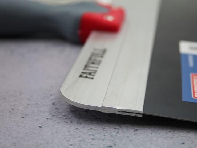 Close-up of the blue steel Faithfull drywall taping knife blade and part of the gray handle with red end.