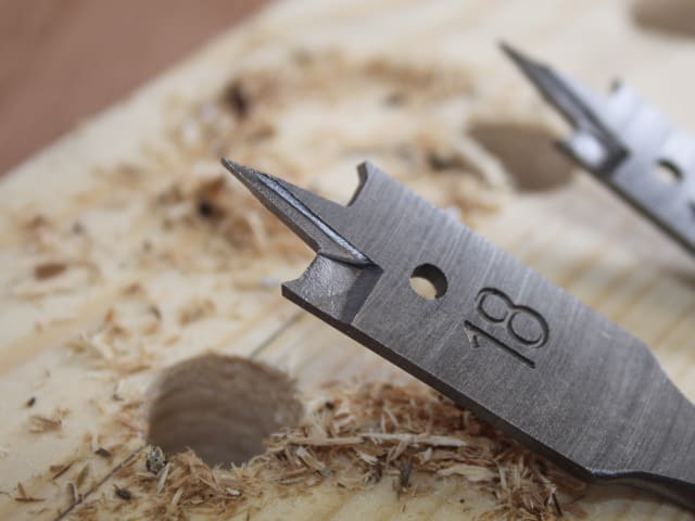 Close-up of a flat bit from the 13-piece Flat Bit Set drilling into wood with wood shavings around.