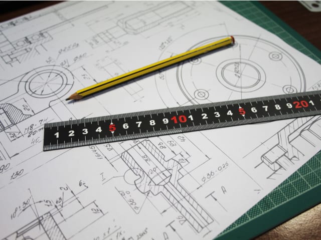 Matt black 300mm measuring rule on technical drawing with yellow pencil on green cutting mat.