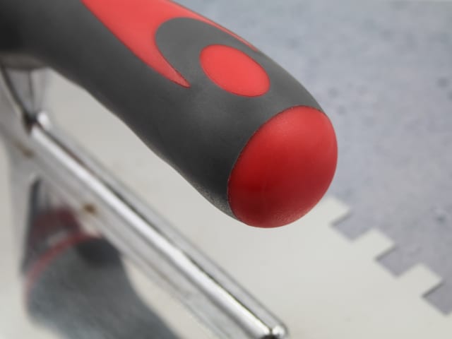 Close-up of the red and black handle and notched edge of the FAI Full Notched Trowel 13