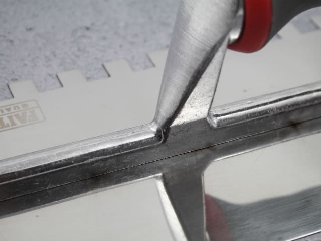 Close-up of the metal handle joint and notched edge of the 13" FAI Full Notched Trowel.