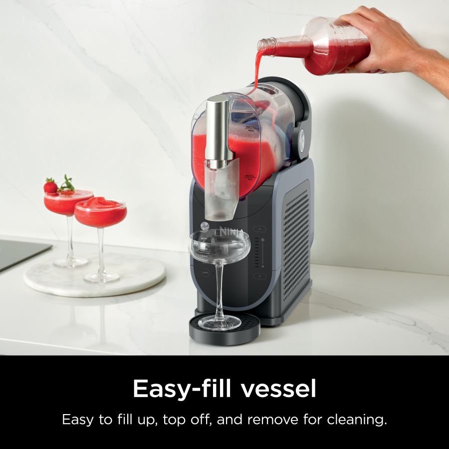 Ninja SLUSHi frozen drink maker with red slush being poured into the easy-fill vessel and glass below.