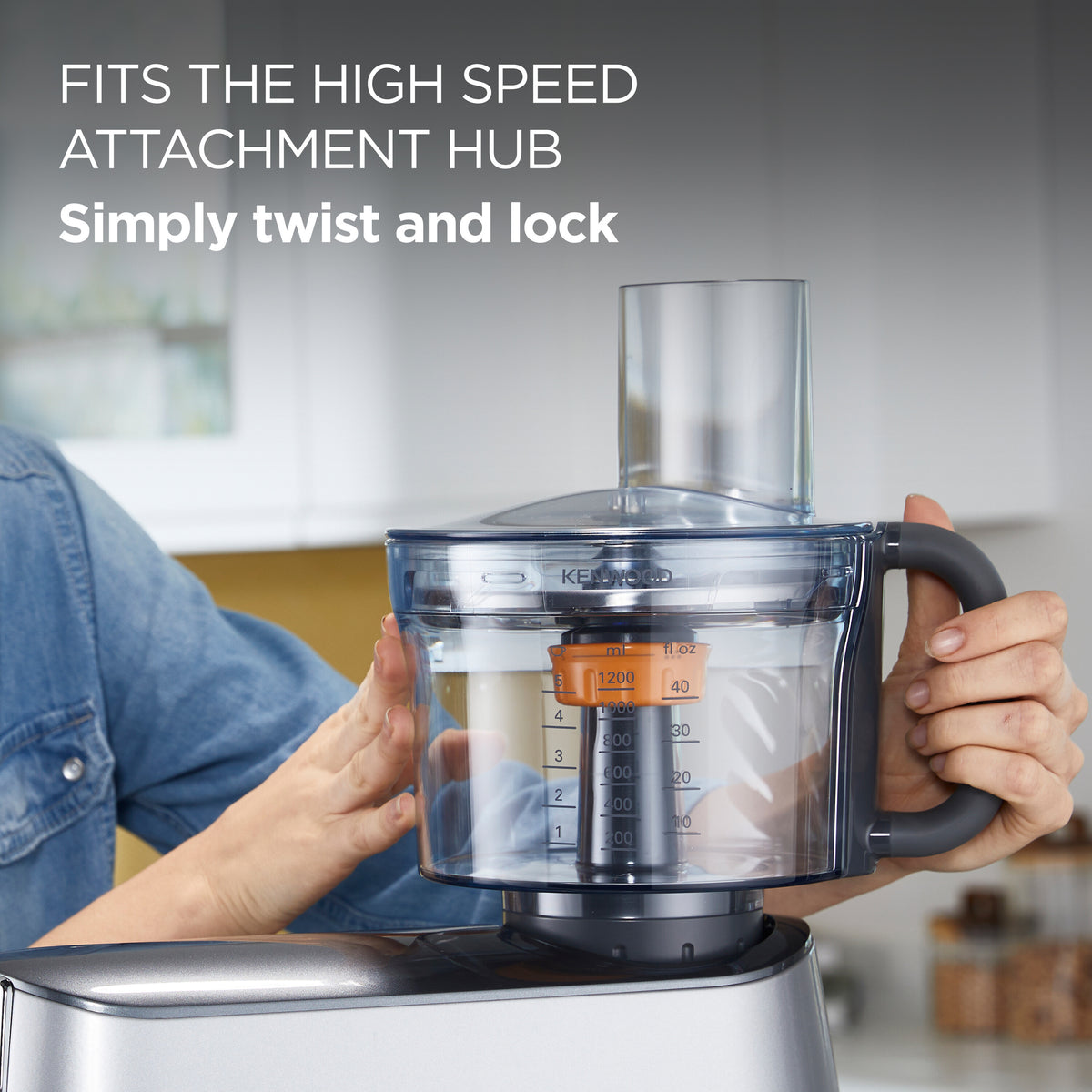Hands holding a Kenwood Chef Food Processor Attachment with clear bowl and measurement markings on a silver base