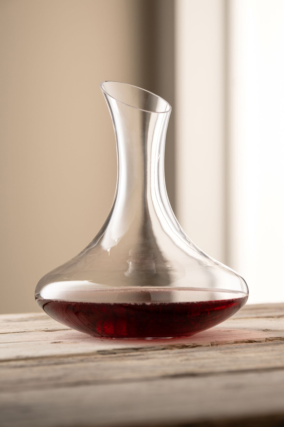 Solus Carafe with a wide base and narrow neck, partially filled with red wine on a wooden surface.