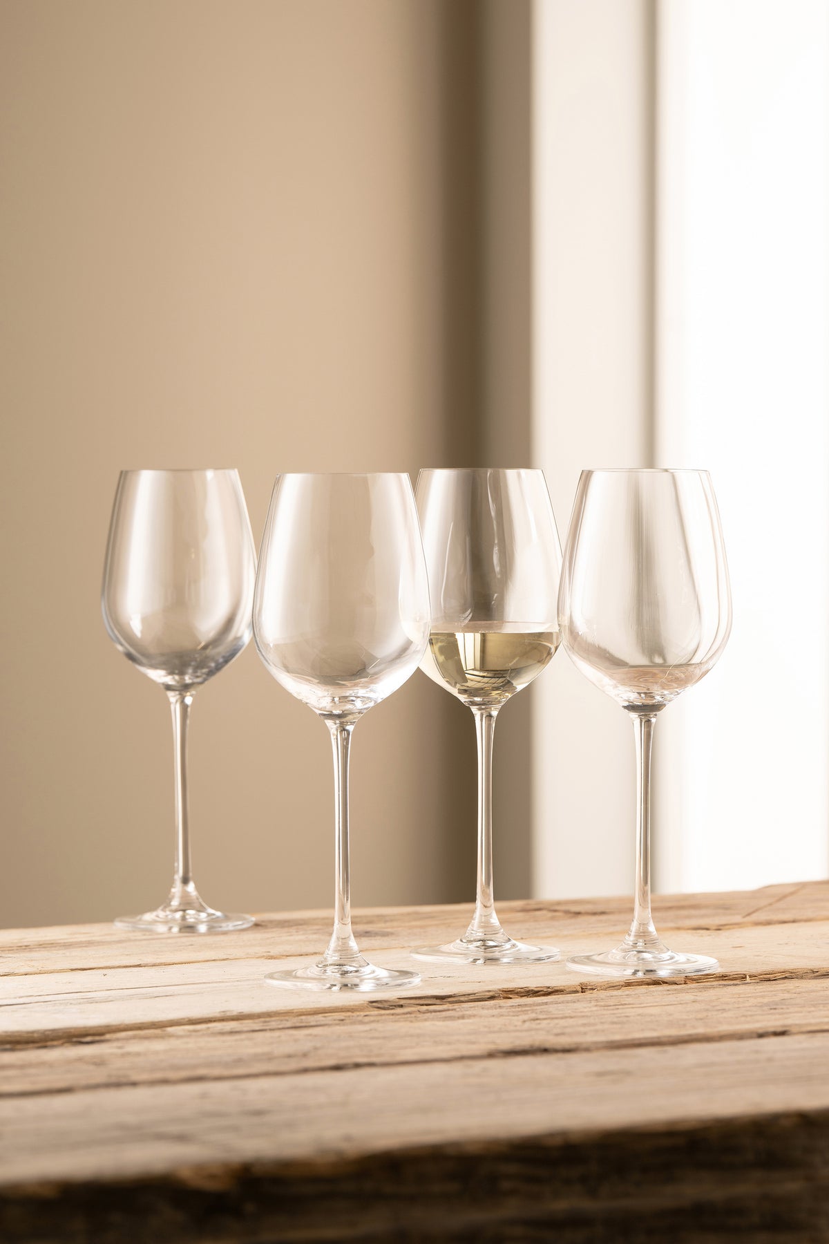 Four clear Solus Wine glasses on a wooden surface, one partially filled with white wine.