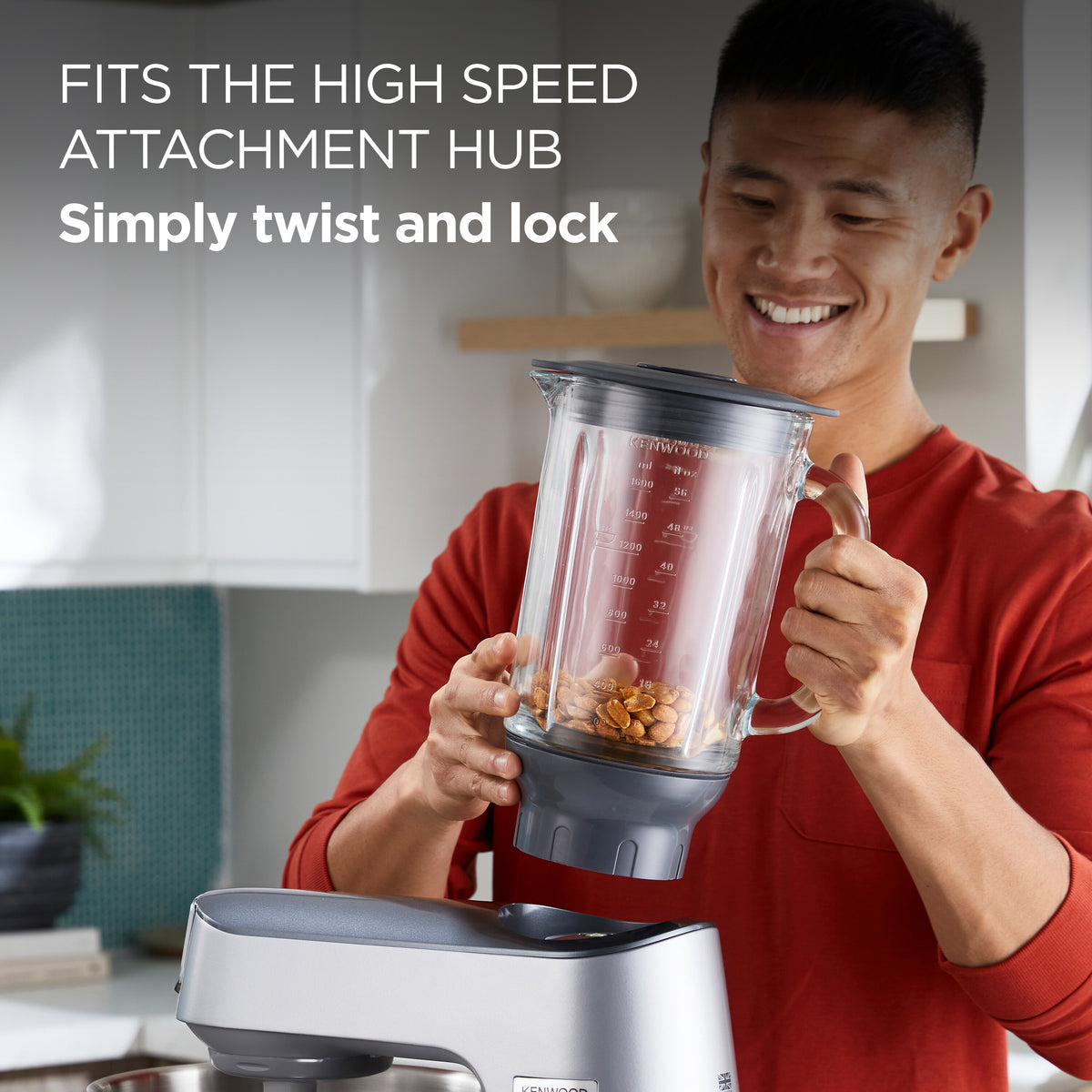 Man holding Kenwood Chef Thermoresist Glass Blender Attachment filled with nuts above mixer base in kitchen