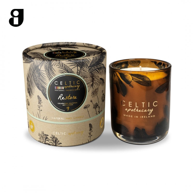 Restore Seagrass Apothecary candle in amber glass with leaf design, next to its botanical-patterned cylindrical box.